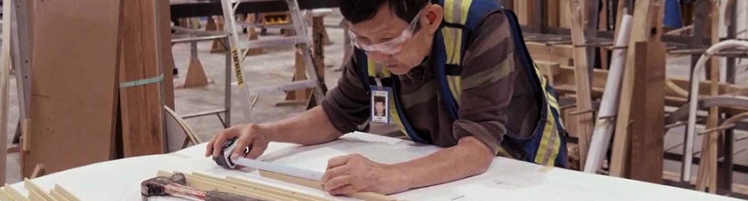 Factory worker measures wood beading for architectural windows