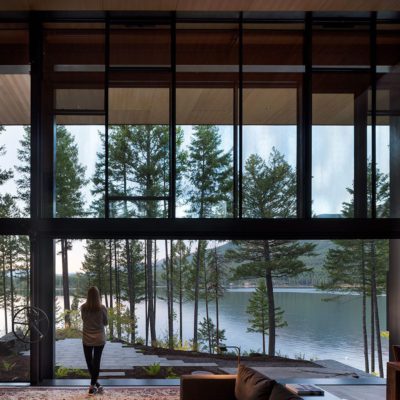 Woman standing by open guillotine window overlooking a lake Olson Kundig designed open guillotine window overlooking a lake